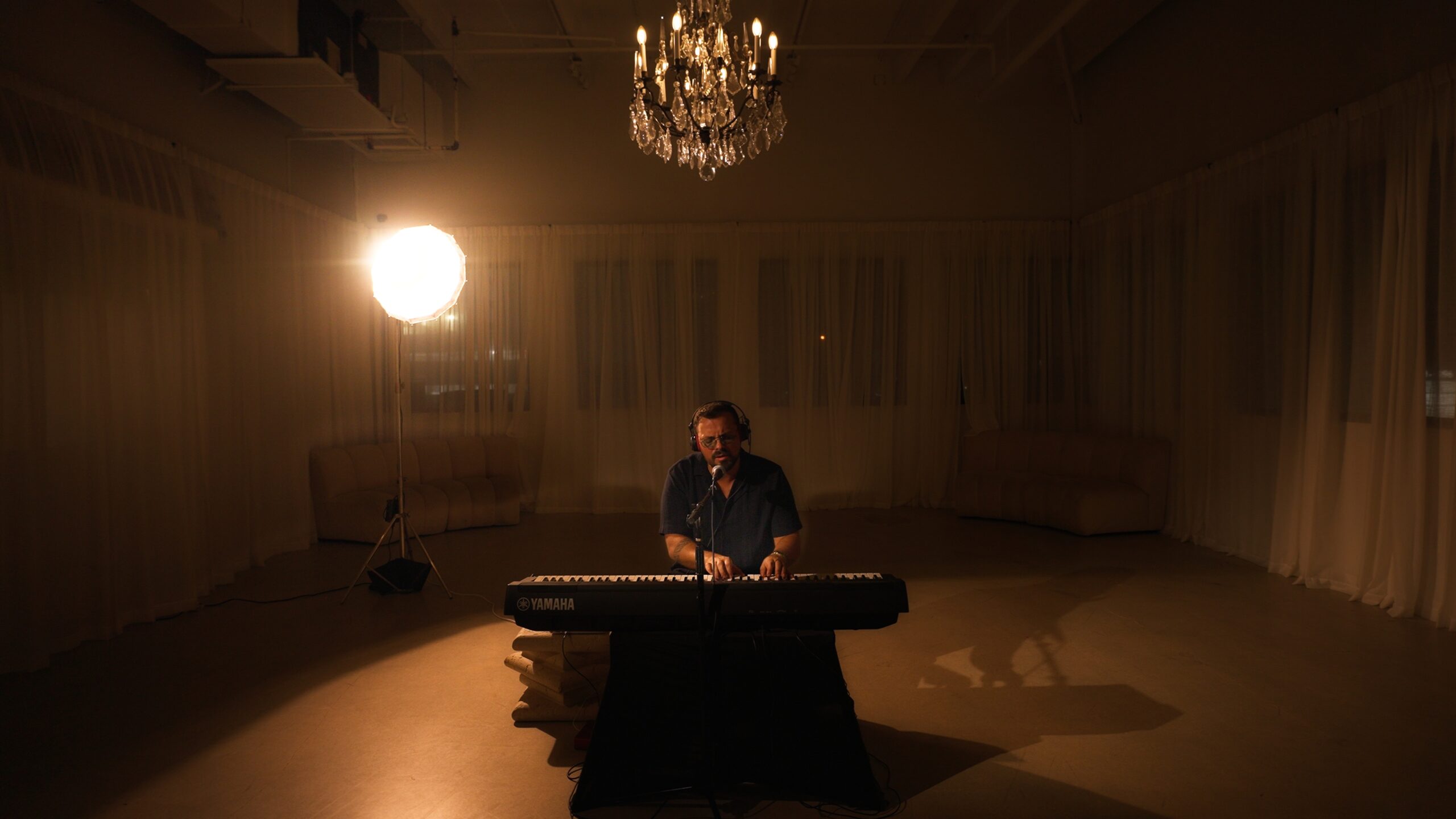 Santiago performing piano and vocals beneath a chandelier